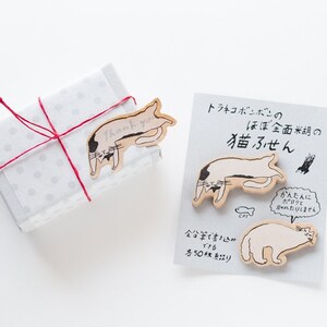 May include: A set of cat-shaped sticky notes with Japanese text that reads "Tra-Neko Bonbon's Almost Full Rice Cat Sticky Notes". The notes are on a white background with a red string and a small gift box.