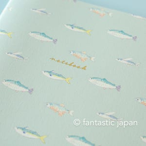 May include: A notebook with a light blue cover featuring a repeating pattern of watercolor-style fish in shades of blue, yellow, and orange. The word "notebook" is written in gold script. The copyright notice "fantastic japan" is at the bottom.