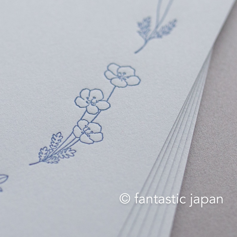 Pode incluir: Uma pilha de papel azul claro com um delicado desenho floral em tinta azul. O desenho apresenta pequenas flores e raminhos, com o texto "fantastic japan" no canto inferior direito.