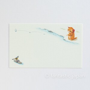 May include: Watercolor illustration of a ginger cat with a red bow, standing near a blue stream. A small bird sits on a rock in the foreground. The image has a light, airy feel with the text "fantastic japan" at the bottom.