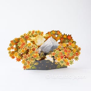May include: A 3D paper art scene depicting Mount Fuji with a full moon and autumn foliage. The artwork features a white mountain peak, a golden moon, and colorful maple leaves in shades of red, orange, and yellow. A white rabbit is also visible.
