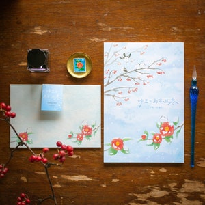 May include: A stationery set featuring a winter theme with a watercolor illustration of birds, red flowers, and falling snow. Includes an envelope, a notepad, a blue glass pen, a stamp, and an inkwell. The text on the envelope reads "ゆきとあそぶ冬".
