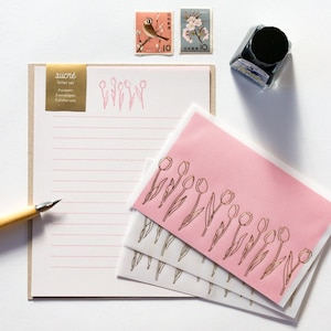 Puede incluir: Un juego de papeler&iacute;a con un sobre rosa y una hoja de papel rayado. El sobre tiene un dise&ntilde;o de tulip&aacute;n dorado y el papel tiene un dise&ntilde;o de tulip&aacute;n dorado en la parte superior. El juego de papeler&iacute;a incluye 4 papeles y 3 sobres.