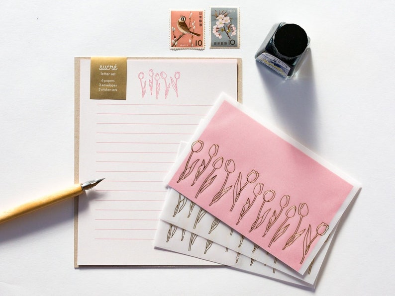 Puede incluir: Un juego de papeler&iacute;a con un sobre rosa y una hoja de papel rayado. El sobre tiene un dise&ntilde;o de tulip&aacute;n dorado y el papel tiene un dise&ntilde;o de tulip&aacute;n dorado en la parte superior. El juego de papeler&iacute;a incluye 4 papeles y 3 sobres.