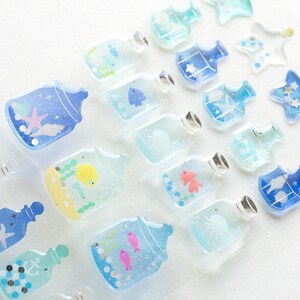 Puede incluir: Surtido de pegatinas de botellas de vidrio azules y transparentes con varios dise&ntilde;os de vida marina, incluyendo peces, estrellas de mar, conchas y anclas. Las pegatinas son perfectas para agregar un toque de fantas&iacute;a a diarios, planificadores y otros proyectos de manualidades.