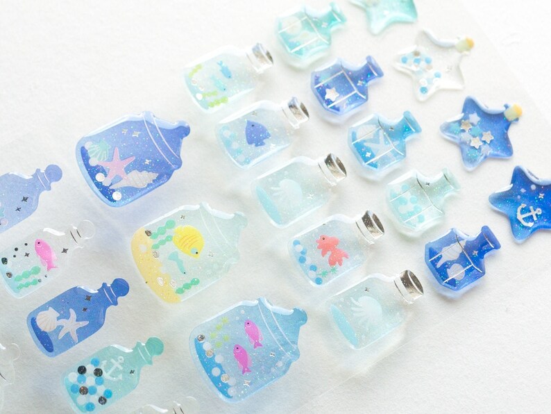 Puede incluir: Surtido de pegatinas de botellas de vidrio azules y transparentes con varios dise&ntilde;os de vida marina, incluyendo peces, estrellas de mar, conchas y anclas. Las pegatinas son perfectas para agregar un toque de fantas&iacute;a a diarios, planificadores y otros proyectos de manualidades.