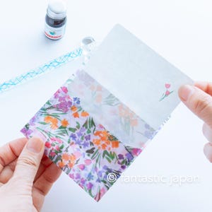 May include: A floral patterned stationery set featuring a translucent envelope with a colorful flower design. The set includes a lined writing card with a tulip illustration and a bottle of ink.