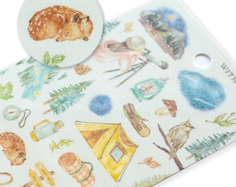 May include: A sheet of stickers with a camping theme. The stickers feature a variety of images, including a tent, a sleeping bag, a compass, a lantern, a deer, a pine tree, a mushroom, an owl, and a starry sky. The stickers are printed on a white background with gold foil accents.