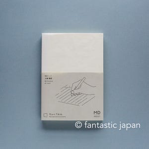 May include: A white notebook with a beige paper band featuring a line drawing of a hand writing on lined paper. The text on the band reads MDノート, 文庫 横罫, MD Notebook, A6 Lined, and 余白は、可能性. Paving moves you forward. The brand name MD PRODUCT is printed in the bottom right corner.