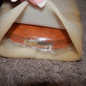 May include: A wooden oval-shaped box with a gold plaque that reads "Celebrating Five Cherished Years". The box is wrapped in clear plastic and surrounded by white foam padding.