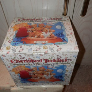 May include: A box for a Cherished Teddies commemorative 5 year anniversary figurine. The box is white with a colorful design and features a picture of five teddy bears in a boat. The text on the box reads "Cherished Teddies Commemorative 5 Year Anniversary Figurine".