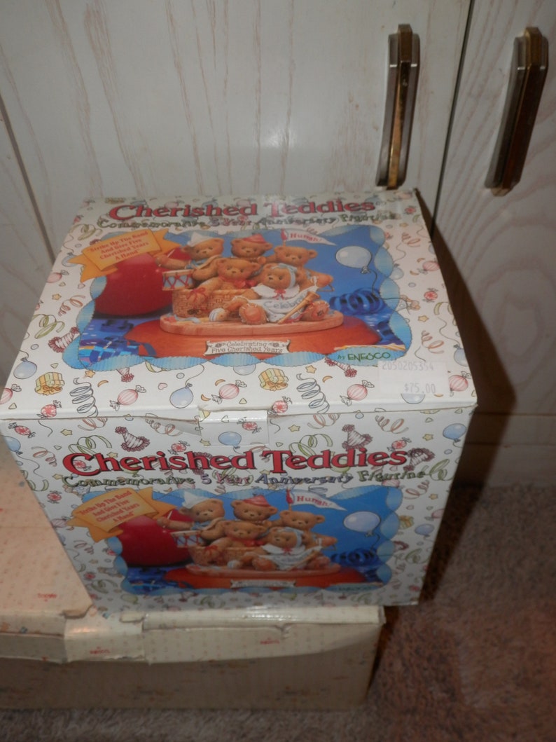 May include: A box for a Cherished Teddies commemorative 5 year anniversary figurine. The box is white with a colorful design and features a picture of five teddy bears in a boat. The text on the box reads "Cherished Teddies Commemorative 5 Year Anniversary Figurine".