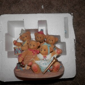 May include: A group of five brown teddy bears wearing party hats and playing musical instruments. The bears are arranged on a wooden base with a banner that reads "Celebrate".