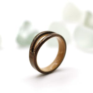 May include: A wooden ring with a split band design. The ring features a dark brown exterior and a lighter wood interior. The ring is a simple, yet elegant piece of jewelry.