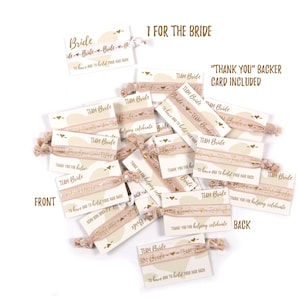May include: A stack of pink and gold hair ties with a white card attached. The card has the text "Team Bride" and "To have and to hold your hair back". The back of the card says "Thank you for helping celebrate".
