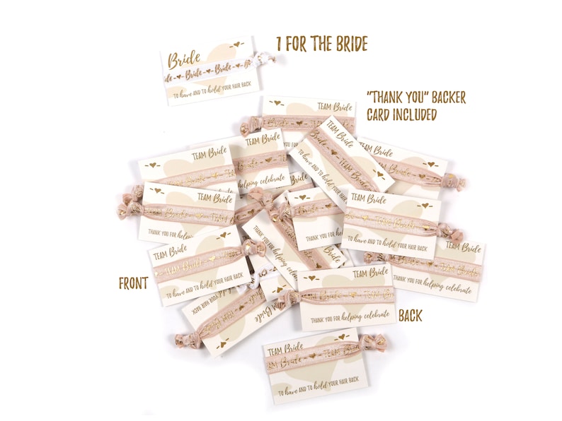 May include: A stack of pink and gold hair ties with a white card attached. The card has the text "Team Bride" and "To have and to hold your hair back". The back of the card says "Thank you for helping celebrate".