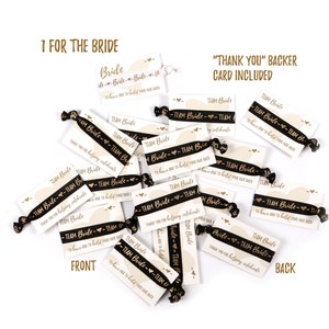May include: A pile of black and gold hair ties with a white card attached to each one. The card says "Team Bride" and "Thank you for helping celebrate".