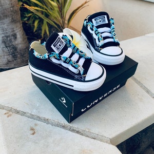 May include: A pair of black Converse All Star sneakers with blue and white beaded laces. The sneakers are in a box with the Converse logo.