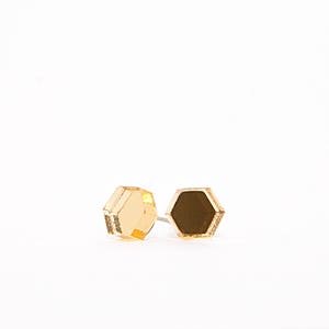 May include: A pair of gold hexagonal stud earrings. The earrings are made of wood and have a mirrored finish.