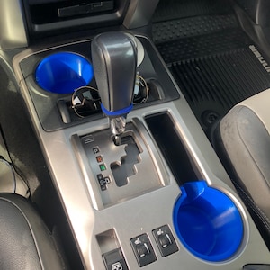 May include: A close-up of the interior of a car with a silver gear shifter, two blue cup holders, and a silver panel with buttons labeled "AUTO" and "S-D".
