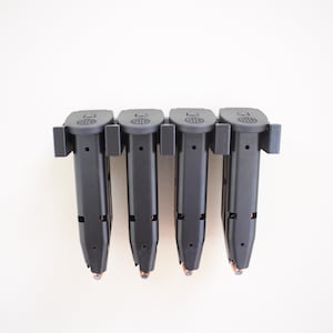 May include: Four black magazine holders with four black magazines inserted. The magazines are mounted on a white wall.