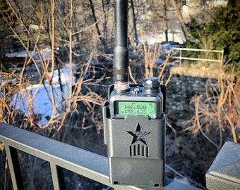 May include: A black two-way radio with a star design on the front. The radio has a green screen displaying the numbers "146.520" and "155.625".