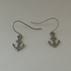 May include: A pair of silver anchor earrings with a simple design. The earrings are made of metal and have a hook fastening.