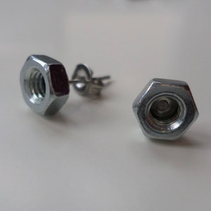 May include: A pair of silver stud earrings made from hexagonal nuts. The nuts have a smooth, metallic finish.