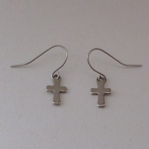 May include: A pair of silver cross earrings with a simple design. The earrings are made of metal and have a hook fastening.