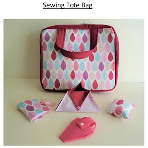 Könnte beinhalten: Eine rote und weiße Näh-Tragetasche mit einem Blatt-Muster. Die Tasche ist offen und zeigt eine rosa und weiße Stofftasche, eine rosa Stoffschere und ein rosa und weißes Stoff-Nadelkissen.