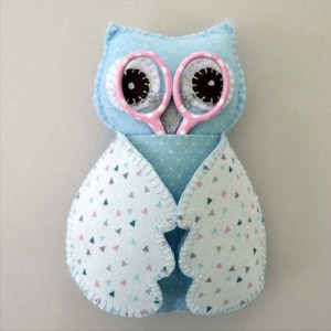 May include: A blue owl-shaped fabric holder with pink and white polka dot eyes and a pair of pink scissors inside.