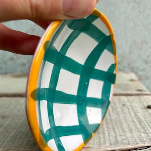 以下が含まれることがあります： 緑と黄色の市松模様が施された、小さな白い陶器のボウル。ボウルは手描きで、わずかに丸みを帯びた形をしています。