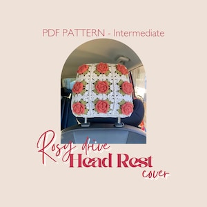 May include: A white crocheted headrest cover with red rose appliqués and green leaves. The cover is attached to a car headrest. Text on the image reads "PDF PATTERN - Intermediate" and "Rosy drive Head Rest cover".