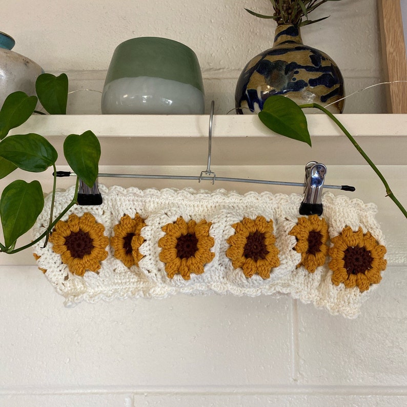 May include: White crocheted sunflower top with a scalloped edge. The top is hanging on a clothes hanger.