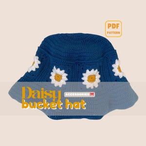 May include: A dark blue crochet bucket hat featuring white daisy motifs with yellow centers. The text on the image reads PDF PATTERN, Daisy bucket hat, and ACCESSORIES. The hat has a wide brim and a textured, hand-stitched appearance.