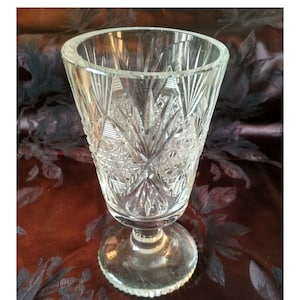 May include: A clear glass vase with a cut glass design. The vase has a wide mouth and a round base.