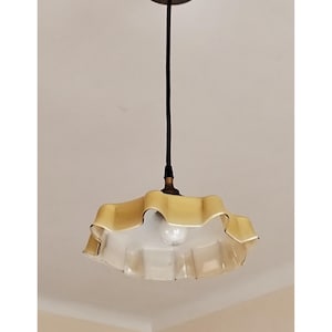 May include: A hanging light fixture with a ruffled, yellow-tinted glass shade. The shade is suspended from a black cord and a silver ceiling mount. The light bulb is visible inside the shade.