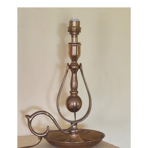 May include: A vintage brass lamp with a decorative, curved handle and a round base. The lamp has a bulb socket at the top and a spherical accent in the center. The lamp is sitting on a white surface.