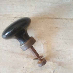 May include: A black ceramic door knob with a brass base and a rusty metal rod.