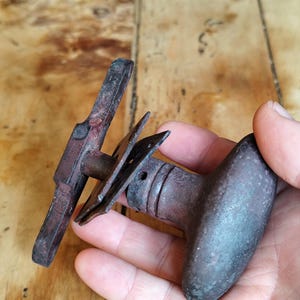 May include: An antique, cast iron door handle set with a dark, aged finish. The set includes a long, rectangular handle and a rounded knob, both showing signs of wear and age. The hardware is likely for a vintage or rustic door.