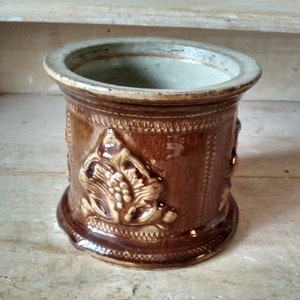 Peut inclure: Un pot en céramique brun avec un motif floral décoratif. Le pot a une large ouverture et une base arrondie.