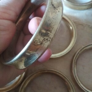 May include: A set of six gold-colored metal rings, likely used as coasters or decorative accents. The rings are smooth and have a slightly worn finish.