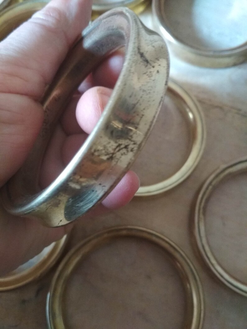 May include: A set of six gold-colored metal rings, likely used as coasters or decorative accents. The rings are smooth and have a slightly worn finish.