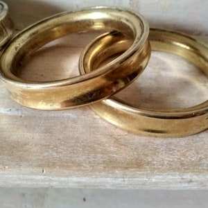 May include: Three gold-colored metal rings, stacked on top of each other. The rings are smooth and have a slightly rounded edge.