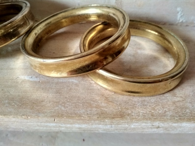 May include: Three gold-colored metal rings, stacked on top of each other. The rings are smooth and have a slightly rounded edge.