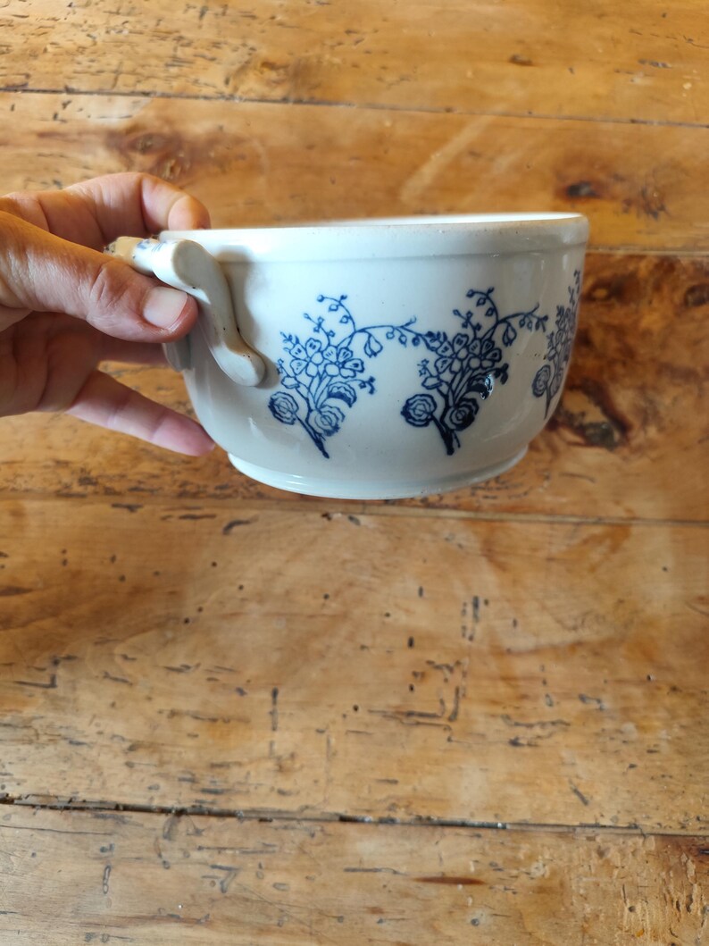Op de afbeelding: Witte keramische kom met een blauw bloemenpatroon en twee handvatten.