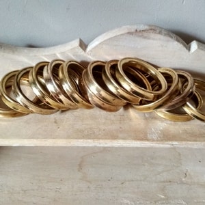 May include: A stack of 15 brass rings, each with a slightly different size and shape. The rings are arranged in a pile, with the largest ring at the bottom and the smallest ring at the top.