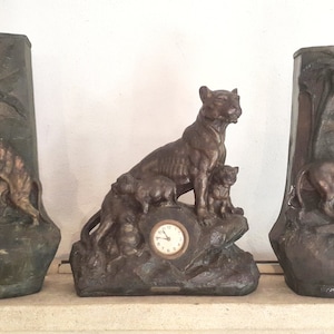 May include: Three decorative bronze vases with animal motifs. The center vase features a lioness with two cubs and a clock face. The left vase features a tiger and the right vase features a lion.