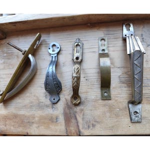 Peut inclure: Diverses poignées de porte anciennes en laiton, argent et bronze. Les poignées sont présentées sur une surface en bois vieilli, mettant en valeur leurs différents designs et finitions. L'image met en évidence la variété des styles.