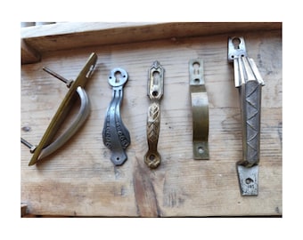 May include: An assortment of vintage door handles in various styles and finishes, including brass, silver, and bronze. The handles are arranged on a weathered wooden surface, showcasing their unique designs and textures.